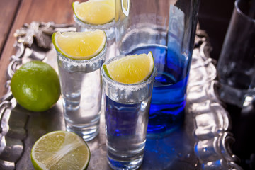 Tequila shot with lime and sea salt and blue bottle on tray