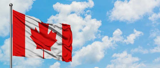 Canada flag waving in the wind against white cloudy blue sky. Diplomacy concept, international relations.