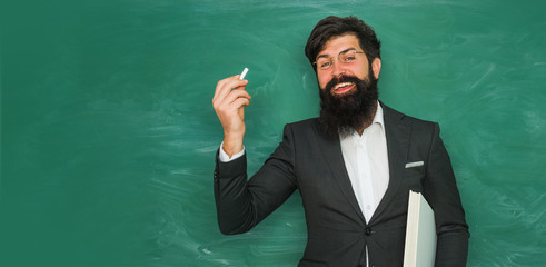 Teacher preparing for university exams. Back to school and happy time. Portrait of male University Student indoors. Young bearded teacher near chalkboard in school classroom.