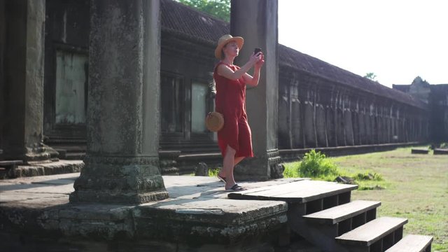 Sliding view of young woman taking photo from porch of Angkor Wat temple built in 12th century in Cambodia and dedicated to Vishnu. Cambodia