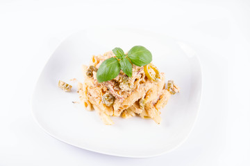 Pasta - penne with white cream sauce with bacon and jalapeño peppers on a plate, decorated with fresh basil