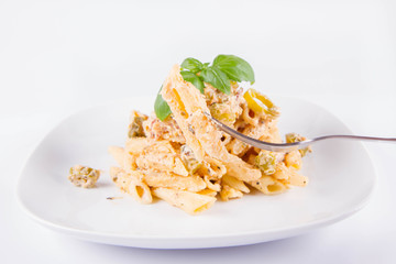 Pasta eaten with a fork - penne with white cream sauce with bacon and jalapeño peppers on a plate, decorated with fresh basil	