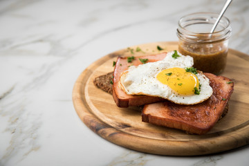 Gebräunter Bayrischer Leberkäse mit gebratenen Spiegelei auf Sonnenblumenkernbrot mit süßen Senf auf Holzbrett