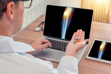 Doctor holding pills with x-ray of leg with pain on the external knee on the laptop and digital tablet. Digital tablet on the wooden desk