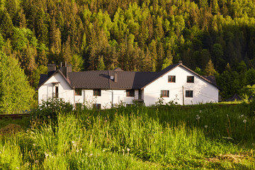 Obraz premium Shot of large white house in bottom of mountains, house situated near forest, guest house in mountains area, place for having rest with friends and family, beautiful landscape. Traveling concept.