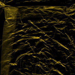 Transparent yellow plastic wrap on the black background. Plastic shopping bag texture. Reusable trash and waste.