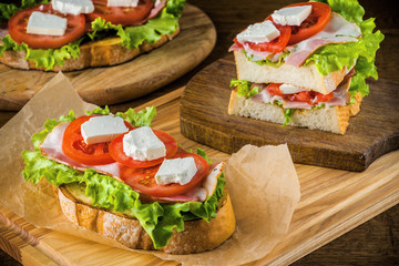 Delicious sandwich and lager beer on wooden table with dark background.