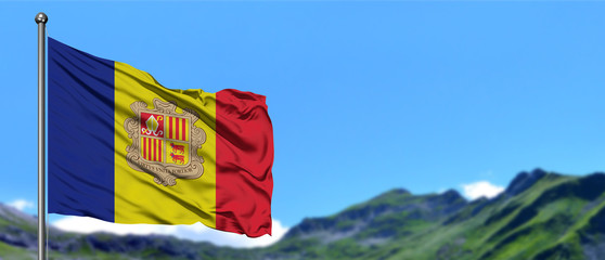 Andorra flag waving in the blue sky with green fields at mountain peak background. Nature theme.