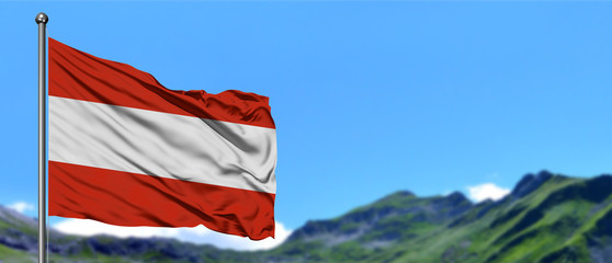 Austria flag waving in the blue sky with green fields at mountain peak background. Nature theme.