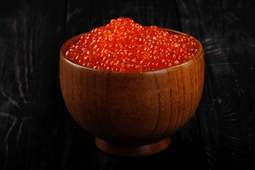 heap of red caviar in wooden cup on wooden background
