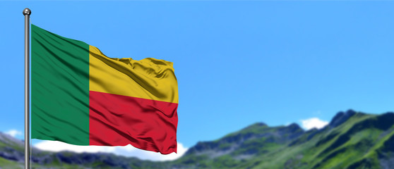 Benin flag waving in the blue sky with green fields at mountain peak background. Nature theme.