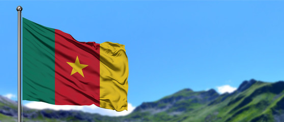 Cameroon flag waving in the blue sky with green fields at mountain peak background. Nature theme.