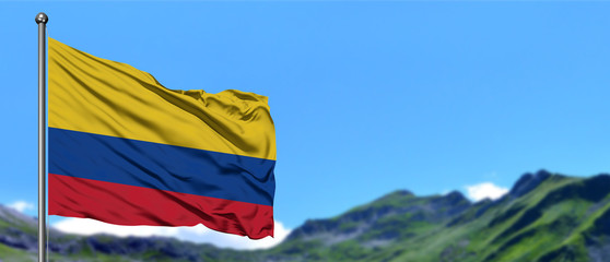 Colombia flag waving in the blue sky with green fields at mountain peak background. Nature theme.