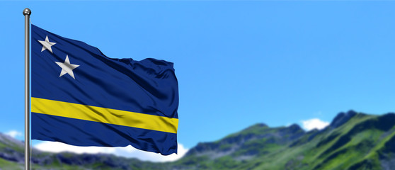 Curacao flag waving in the blue sky with green fields at mountain peak background. Nature theme.