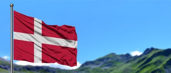 Denmark flag waving in the blue sky with green fields at mountain peak background. Nature theme.