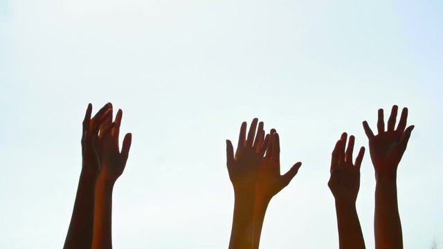 Tracking shot of several human hands raised against the sky
