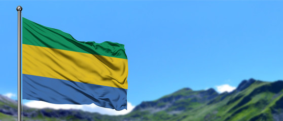 Gabon flag waving in the blue sky with green fields at mountain peak background. Nature theme.