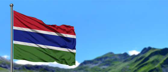 Gambia flag waving in the blue sky with green fields at mountain peak background. Nature theme.