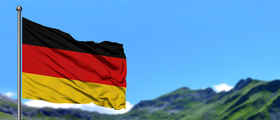 Germany flag waving in the blue sky with green fields at mountain peak background. Nature theme.