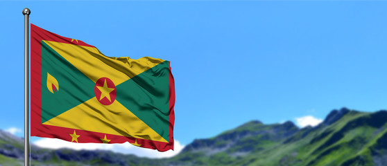 Grenada flag waving in the blue sky with green fields at mountain peak background. Nature theme.