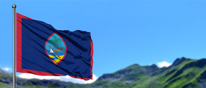 Guam flag waving in the blue sky with green fields at mountain peak background. Nature theme.
