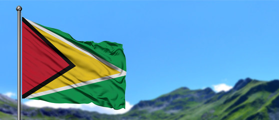 Guyana flag waving in the blue sky with green fields at mountain peak background. Nature theme.