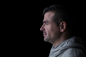 Side studio portrait of a serious man looking sideways. Isolated on black background. Horizontal. Copyspace.