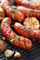 Grilling sausages with the addition of herbs and vegetables on the grill plate, close-up. Grilling...