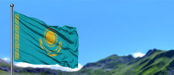 Kazakhstan flag waving in the blue sky with green fields at mountain peak background. Nature theme.