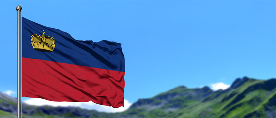 Liechtenstein flag waving in the blue sky with green fields at mountain peak background. Nature theme.