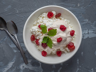 Breakfast from homemade cottage cheese with sour cream of melted cream with berries dried cherries in a deep white plate, on a gray background, two teaspoons. Shot with close-up, top view.