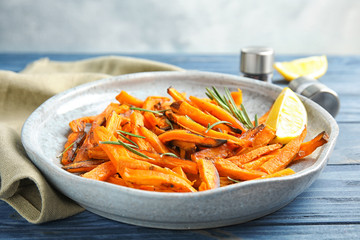 Plate with baked sweet potato slices, rosemary and lemon on wooden table, closeup