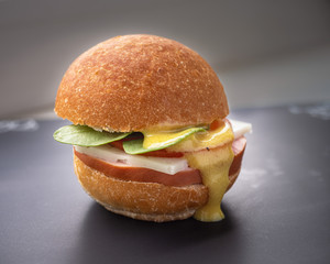 Hamburger with sausage, cheese and tomato, arugula, topped with sauce.