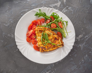 Light breakfast of omelet and cherry tomato on a large white plate, shot from close range, top view.