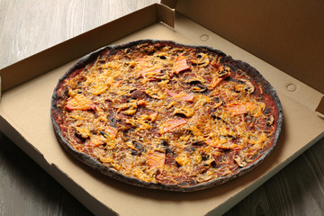 Box with black pizza on table, closeup
