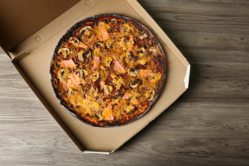 Box with black pizza on wooden table, top view