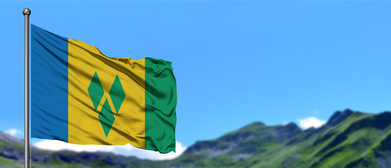 Saint Vincent And The Grenadines flag waving in the blue sky with green fields at mountain peak...