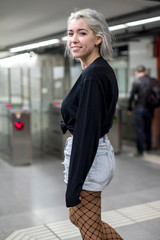 Back view of a young woman in shorts holding a long board while standing on mechanic stairs at night