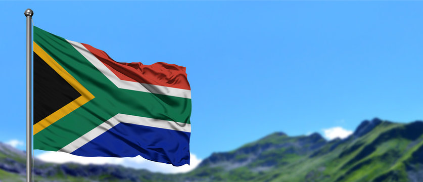 South Africa flag waving in the blue sky with green fields at mountain peak background. Nature theme.