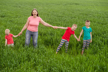 Fototapeta na wymiar Happy mother with children playing on a green field with wheat..Unity with nature concept