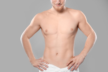 Young man with slim body in towel on grey background, closeup