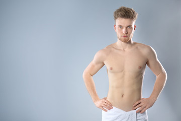 Fototapeta na wymiar Portrait of young man with slim body in towel on grey background. Space for text