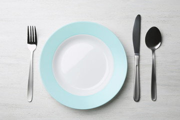 Stylish ceramic plate and cutlery on white wooden background, flat lay