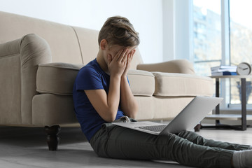 Frightened little child with laptop in room. Danger of internet