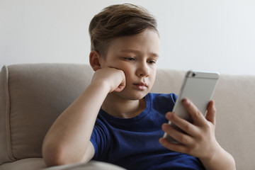 Little child with smartphone on sofa in room. Danger of internet