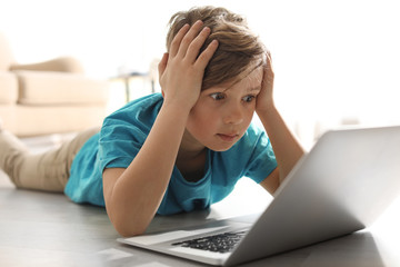 Shocked little child with laptop on floor indoors. Danger of internet