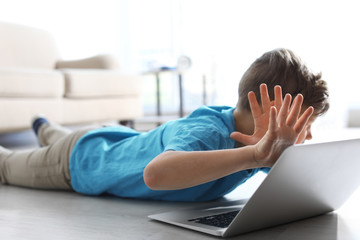 Frightened little child with laptop on floor indoors. Danger of internet