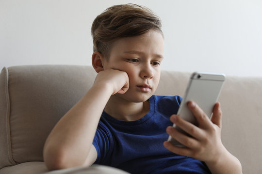 Little Child With Smartphone On Sofa In Room. Danger Of Internet