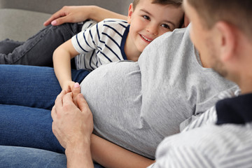 Fototapeta premium Pregnant mother, father and son spending time together on sofa at home. Family time