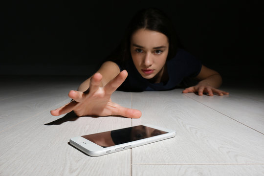 Lonely woman reaching out for smart phone on floor indoors. Internet addiction